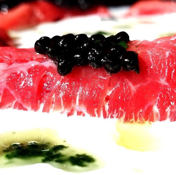 Rotllets de carpaccio de vedella amb crema agra, perles de trufa negra i oli de ruca