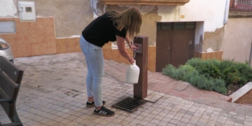 Una veïna de Prat de Comte omple garrafes d’aigua en una font del municipi